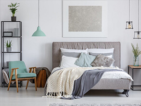 Crisp white bedroom with cosy white and grey blankets and green chair and light with plants table